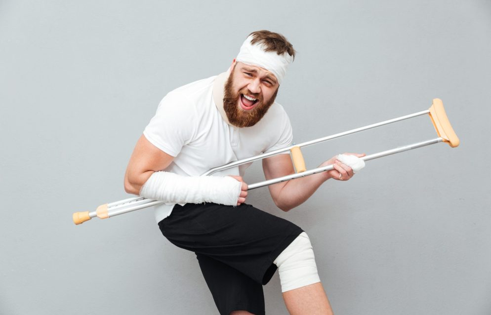 Cheerful playful young man having fun with crutch over white background